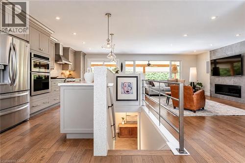 Wood-finish flooring throughout, kitchen with stainless steel appliances, modern lighting fixtures, built-in fireplace, and a stone-clad accent wall - 896 Eagle Drive, Burlington, ON 