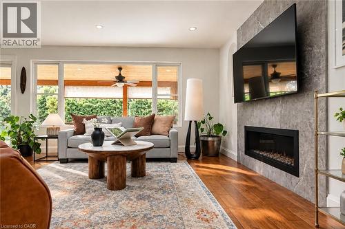 Stone-clad fireplace with an integrated linear firebox, rich wood-finish flooring, recessed lighting, and expansive windows - 896 Eagle Drive, Burlington, ON 