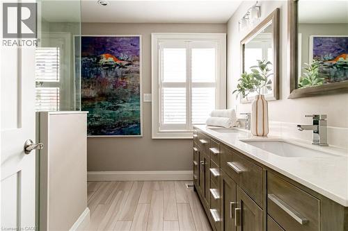 Dual vanity with chrome fixtures and white countertop, wood-finish flooring, glass-enclosed shower, and window with plantation shutters - 896 Eagle Drive, Burlington, ON 
