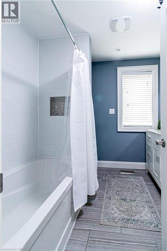 Tub and shower combination with white subway tile surround, mosaic tile shower niche, wood-finish flooring, and white vanity with lower cabinetry - 896 Eagle Drive, Burlington, ON 