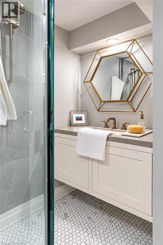 Floating vanity with a light-toned countertop, hexagonal wall mirror with a gold-finish frame, and white hexagonal floor tiles - 896 Eagle Drive, Burlington, ON 