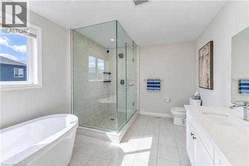 Freestanding soaking tub, glass-enclosed shower with tiled walls and pebble-finish floor, single vanity with integrated sink and chrome faucet, and light-toned tile flooring - 365 Woolwich Street, Waterloo, ON 