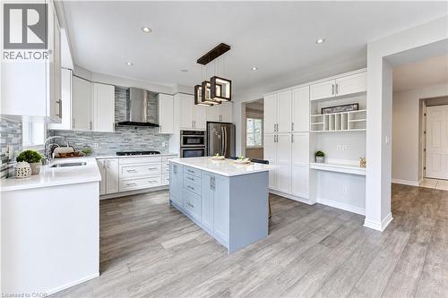 Contemporary kitchen featuring white cabinetry, a blue central island with a solid surface countertop, stainless steel appliances, a tile backsplash, and wood-finish flooring - 365 Woolwich Street, Waterloo, ON 