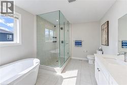 Freestanding soaking tub, glass-enclosed shower with tiled walls and pebble-finish floor, single vanity with integrated sink and chrome faucet, and light-toned tile flooring - 