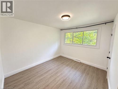 Wood-finish flooring with white baseboards, a flush-mount ceiling light, a multi-pane window, and a white door with dark hardware - 84 Weber Street S, Waterloo, ON 