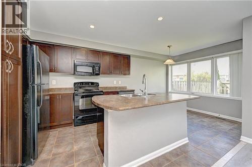Kitchen featuring dark wood cabinetry, a center island with sink and integrated breakfast bar, black appliances, and tiled flooring - 103 Blackbird Circle, Cambridge, ON 
