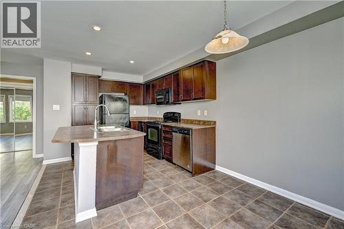 Kitchen featuring dark wood-finish cabinetry, a built-in pantry, stainless steel appliances, an island with an integrated sink, and tile flooring - 103 Blackbird Circle, Cambridge, ON 