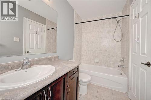 Built-in vanity with a single basin sink, laminate countertop, dark wood-finish cabinetry, tiled shower surround, and tiled flooring - 103 Blackbird Circle, Cambridge, ON 
