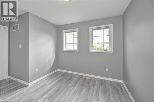 Wood-finish flooring with crisp white trim, two windows with grid detailing, and a flush mount ceiling light - 103 Blackbird Circle, Cambridge, ON 