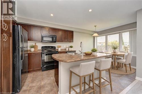 Rich wood-finish cabinetry, black appliances, a central island with an integrated sink, and an adjacent dining area with broad windows - 103 Blackbird Circle, Cambridge, ON 