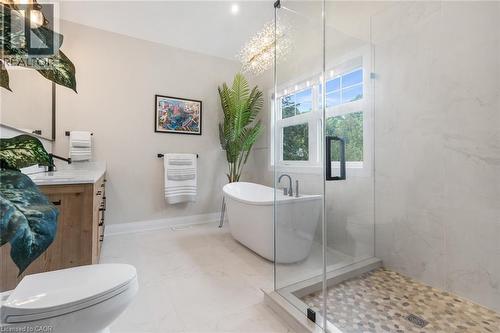 Freestanding soaking tub, glass-enclosed shower with pebble-tile floor, wood-finish vanity with stone countertop, and contemporary chandelier - 293 North Shore Boulevard E, Burlington, ON 