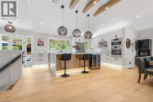 Modern kitchen featuring wood-finish flooring, white cabinetry, a center island with seating, integrated appliances, and exposed ceiling beams - 293 North Shore Boulevard E, Burlington, ON 