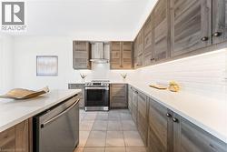 Kitchen featuring backsplash, appliances with stainless steel finishes, light tile patterned flooring, wall chimney exhaust hood, and light stone countertops - 