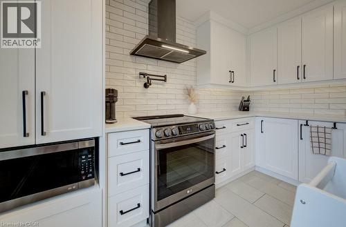 White shaker-style cabinetry with black hardware, stainless steel appliances, light-toned subway tile backsplash, white countertops, and light-toned tile flooring - 37 Margaret Avenue N, Waterloo, ON 