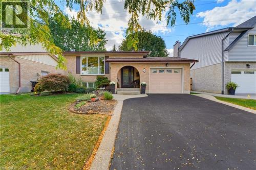 Brick exterior with an arched entry, an attached garage, a paved driveway, and mature landscaping - 77 Yellow Birch Drive, Kitchener, ON 