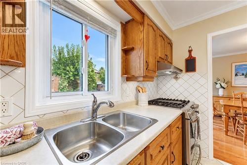Double stainless steel sink, wood cabinetry, tile backsplash, built-in gas range, and a window with natural light - 104 Deerwood Crescent, Kitchener, ON 