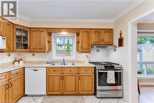 Wood-finish cabinetry, stainless steel range and hood, white dishwasher, double basin sink, and tile backsplash - 104 Deerwood Crescent, Kitchener, ON 