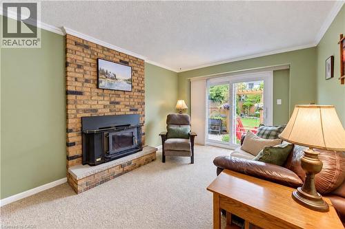Brick-clad fireplace with a wood-burning insert, crown molding, and sliding glass doors leading to the outdoor space - 104 Deerwood Crescent, Kitchener, ON 
