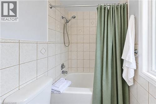 Bathtub and shower combination featuring a flexible showerhead, tiled surround with decorative accents, and a window providing natural light - 104 Deerwood Crescent, Kitchener, ON 