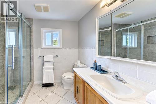 Glass-enclosed shower, wood-finish vanity with an integrated sink, built-in medicine cabinet, and tiled walls and flooring - 104 Deerwood Crescent, Kitchener, ON 