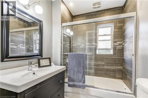 Vanity with integrated sink, framed mirror, wall-mounted light fixture, and tiled shower with glass enclosure - 11 Elm Street, Hamilton, ON 