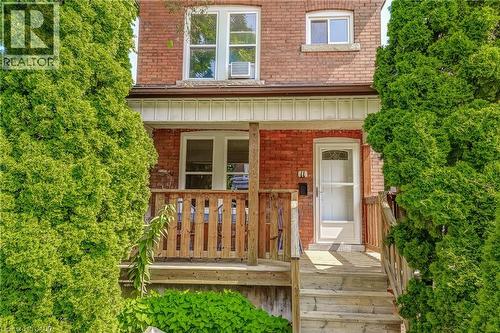 Brick exterior with a covered porch, wood-finish railing, and mature evergreen plantings - 11 Elm Street, Hamilton, ON 