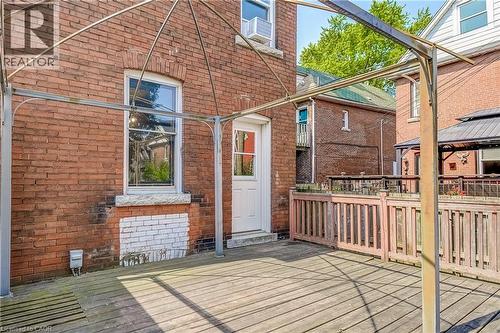 Outdoor wood-decked patio featuring a metal pergola frame, brick exterior, and a white door with transom window - 11 Elm Street, Hamilton, ON 