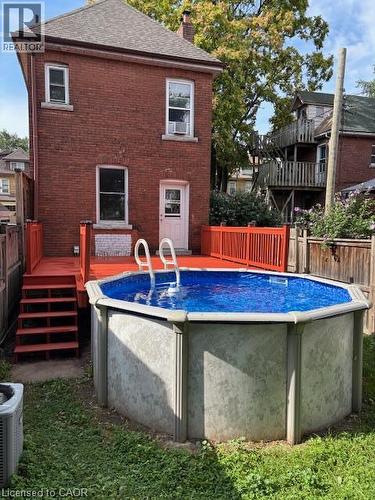 Red brick exterior featuring an above-ground pool, a red-painted deck, and exterior stairs - 11 Elm Street, Hamilton, ON 
