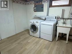 Laundry area featuring light wood-finish flooring, a utility sink, and white paneled walls - 