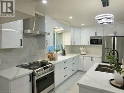 Modern kitchen featuring glossy white cabinetry, stainless steel appliances, quartz countertops, and a contemporary pendant light fixture - 