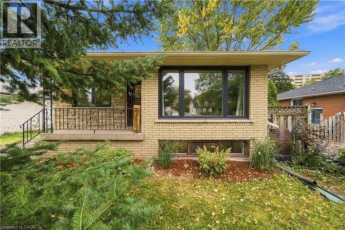 Light-colored brick exterior with dark-framed windows, a concrete front porch, and decorative wrought iron railings - 662 Dynes Road, Burlington, ON 