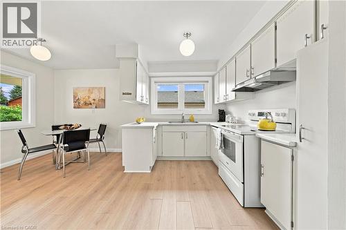 White cabinetry with brushed nickel hardware, light wood-finish flooring, white appliances, and a window above the sink - 662 Dynes Road, Burlington, ON 