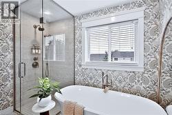 Freestanding soaking tub with floor-mounted faucet, glass-enclosed shower with tile surround, and patterned wallpaper - 