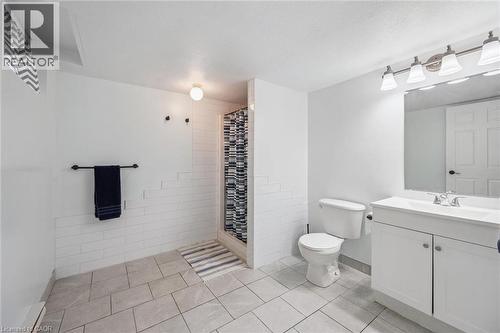 Spacious bathroom featuring tiled flooring, a shower stall with white subway tile surround, a white vanity with an integrated sink, and an overhead vanity light fixture - 233 Dearborn Boulevard, Waterloo, ON 