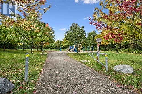 Paved pathway surrounded by mature trees, leading to a playground area with visible equipment - 233 Dearborn Boulevard, Waterloo, ON 