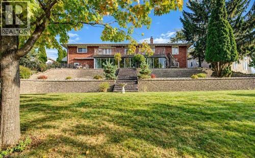 Walkout basement with expansive backyard with a tiered retaining wall leading to a brick-clad residence featuring a sunroom and multiple upper-level balconies - 1370 Thorman Place, Cambridge, ON 