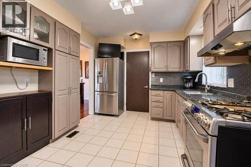 Kitchen featuring tile flooring, a dark mosaic tile backsplash, perimeter cabinetry with varied finishes, and stainless steel appliances - 1370 Thorman Place, Cambridge, ON 