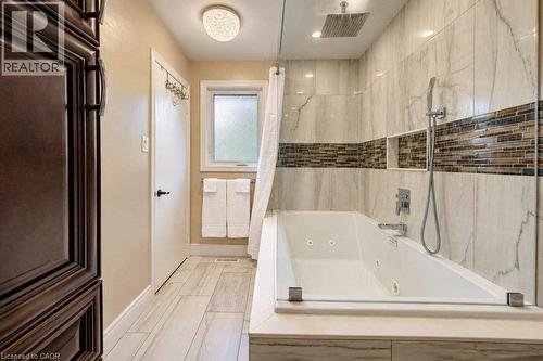 Soaking tub with integrated jets, glass shower panel, tiled shower surround with mosaic accent, rainfall shower head, and wood-finish flooring - 1370 Thorman Place, Cambridge, ON 