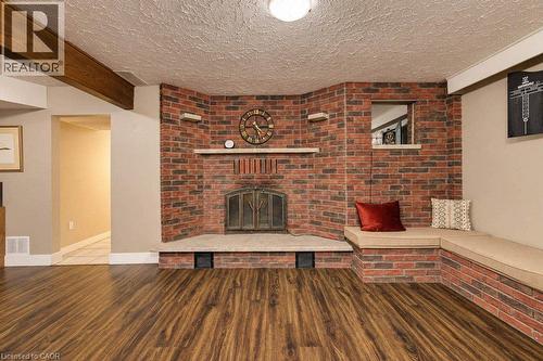 Brick fireplace with hearth, built-in corner seating, wood-finish flooring, and exposed ceiling beam - 1370 Thorman Place, Cambridge, ON 