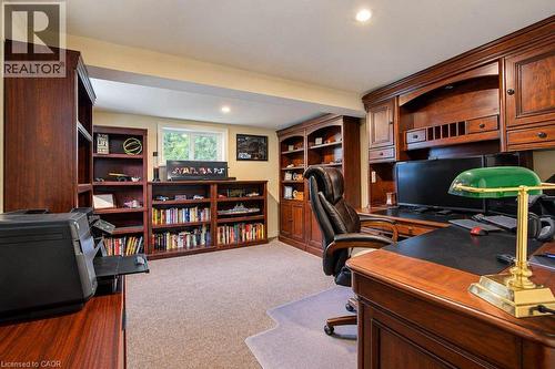 Sophisticated home office featuring rich wood-finish cabinetry, built-in shelving with display storage, desk workspace with task lighting, plush seating, and carpet flooring - 1370 Thorman Place, Cambridge, ON 