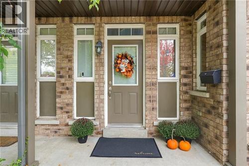 Brick façade with a covered front porch, featuring a panel-style entry door and flanking sidelight windows with transom details - 1076 Ryckman Common, Burlington, ON 