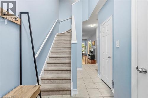 Entryway featuring light blue walls, tiled flooring, carpeted staircase with a white handrail, and a white paneled door - 1076 Ryckman Common, Burlington, ON 