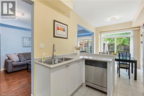 Kitchen with a double basin stainless steel sink, stainless steel dishwasher, white cabinetry, and light-toned countertops - 1076 Ryckman Common, Burlington, ON 