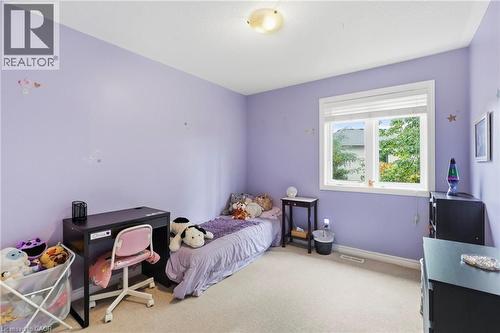 Carpeted room with a ceiling-mounted light fixture, a window with white trim, and light purple painted walls - 1076 Ryckman Common, Burlington, ON 