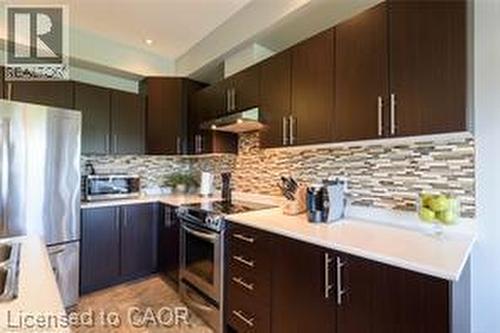 Kitchen featuring dark wood-finish cabinetry, white countertops, a mosaic tile backsplash, and stainless steel appliances - 28 Madonna Drive, Hamilton, ON 