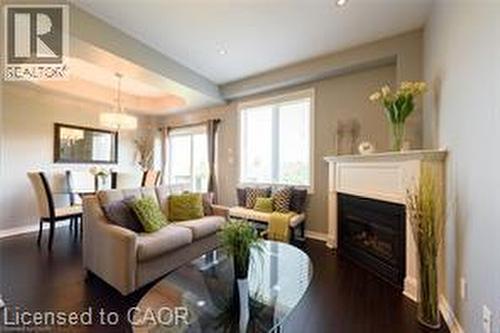 Dark wood-finish flooring, tray ceiling with recessed lighting, fireplace with mantel, and large window - 28 Madonna Drive, Hamilton, ON 