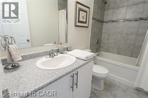 Vanity with a speckled countertop and integrated sink, chrome faucet, white cabinetry with dark pull handles, and a white bathtub with subway tile surround and decorative accent band - 28 Madonna Drive, Hamilton, ON 