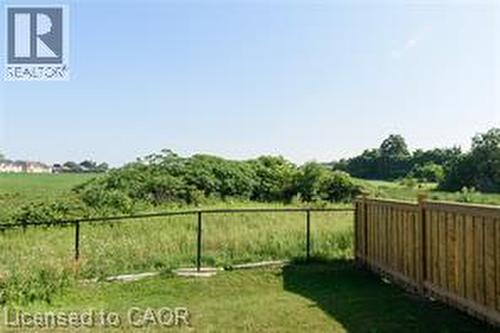 Expansive grassy area featuring a black metal fence and a wood plank fence - 28 Madonna Drive, Hamilton, ON 