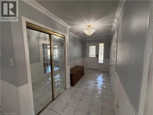 Tiled flooring, wainscoting, crown molding, double front entry doors with decorative glass, and a ceiling-mounted light fixture - 37 Elora Drive, Hamilton, ON 