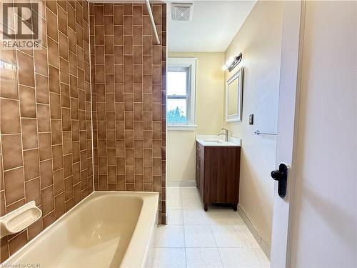 Tiled shower surround, built-in bathtub, wood-finish vanity with integrated sink, wall-mounted mirror, and tiled flooring - 507 Aberdeen Avenue, Hamilton, ON 